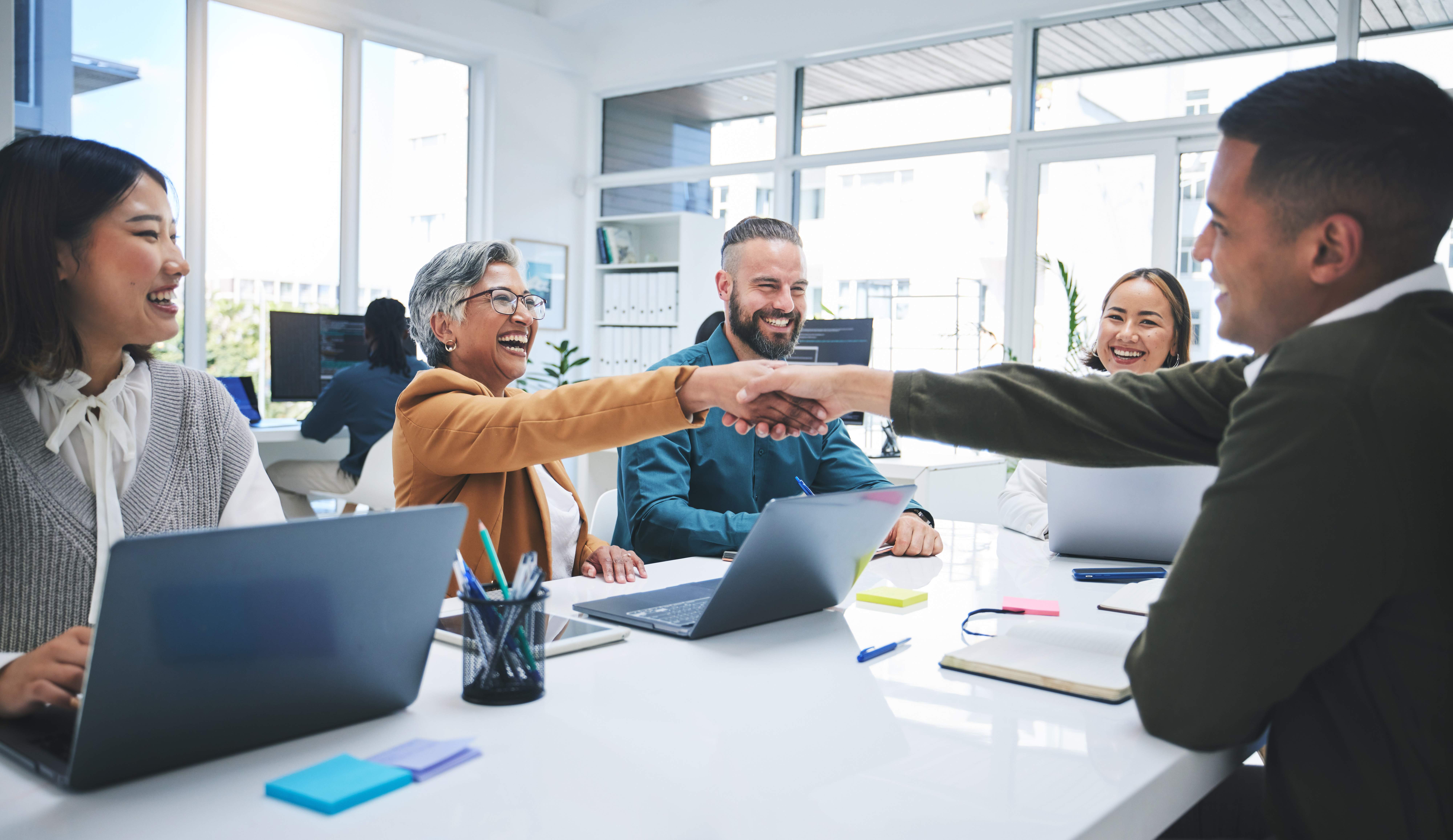 Diverse professionals smiling and shaking hands during a meeting in a bright modern office